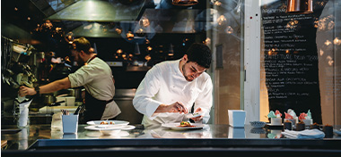 A chef cooking in his restaurant's kitchen with his employees