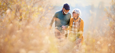 Happy senior couple taking an autumn walk through tall grass in nature.