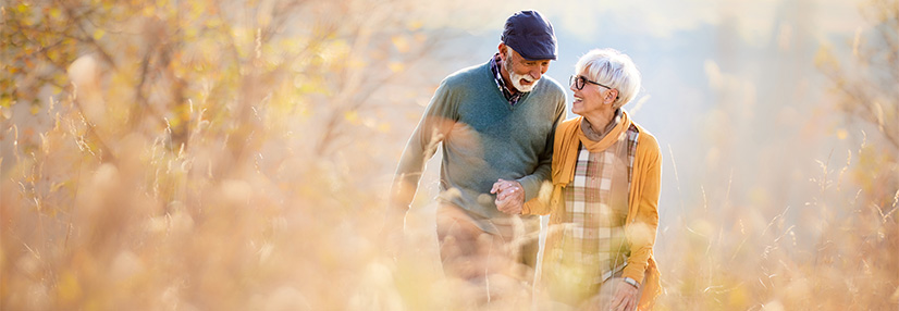 Happy senior couple taking an autumn walk through tall grass in nature.