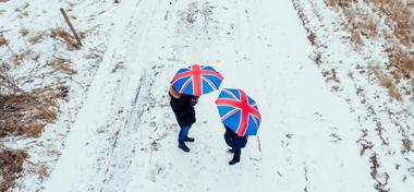 Couple walking together in snowy landscape holding British Union Jack umbrellas 