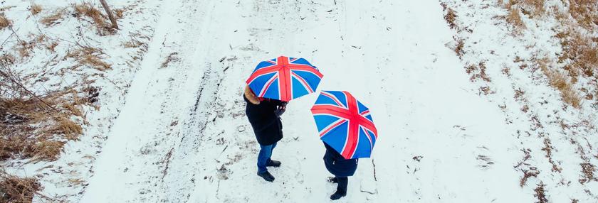 Couple walking together in snowy landscape holding British Union Jack umbrellas 