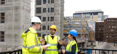 Three construction employees standing together outside a construction site