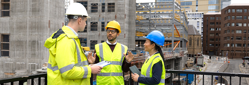 Three construction employees standing together outside a construction site