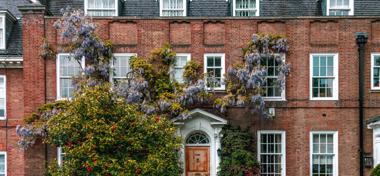 Charming Georgian Red Brick Townhouse Entrance with Wooden Door and Blooming Wisteria Garden in Spring in London