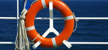 Ship railing and red life ring foreground, blue sea background