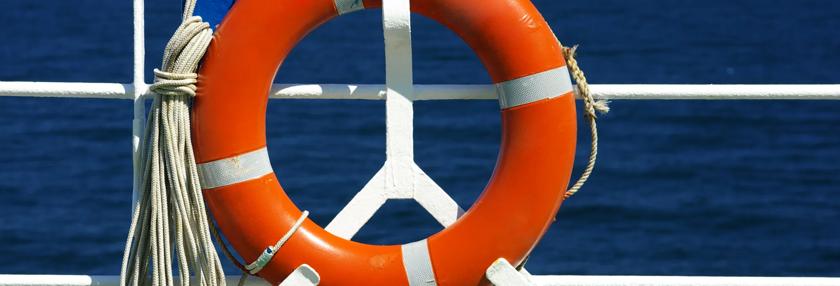 Ship railing and red life ring foreground, blue sea background