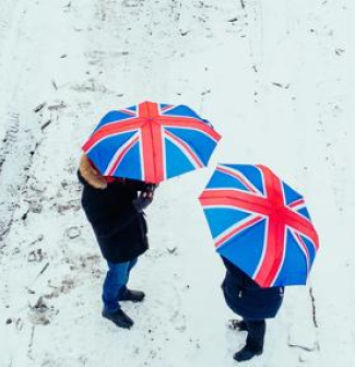 Couple walking together in snowy landscape holding British Union Jack umbrellas 